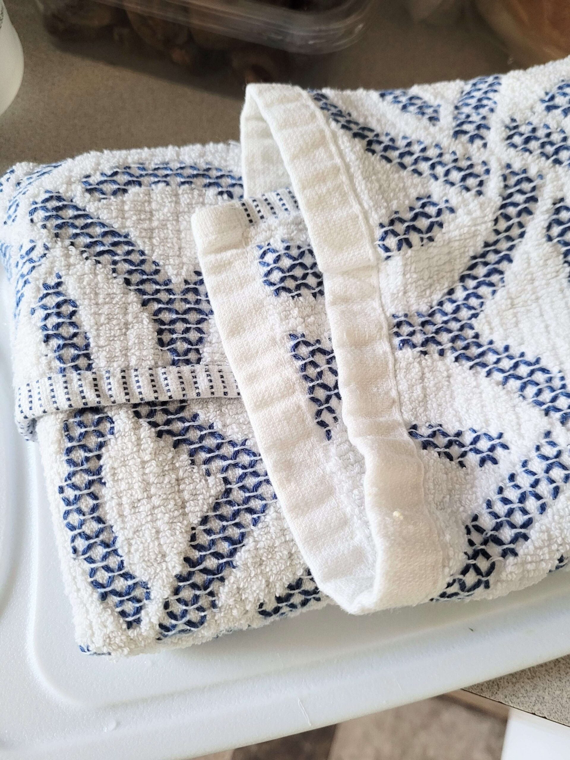 Tofu wrapped in a white and blue towel on a white cutting board.
