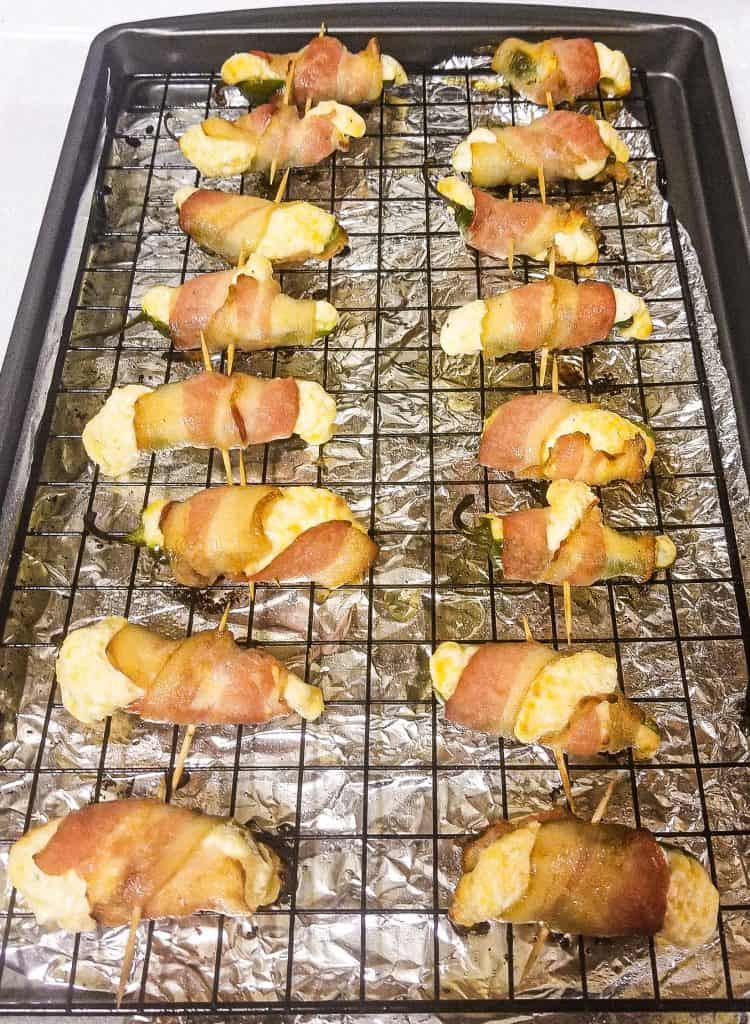 bacon wrapped jalapenos on a wire rack going into the oven.