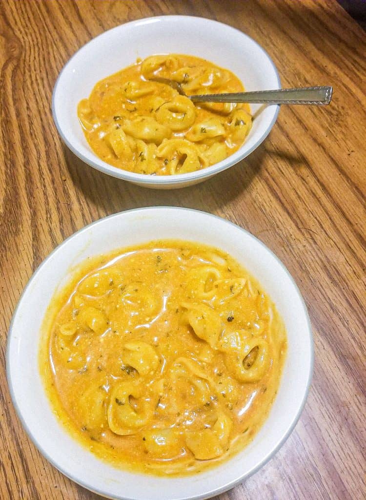 tomato soup with tortellini in bowls on a brown table. 