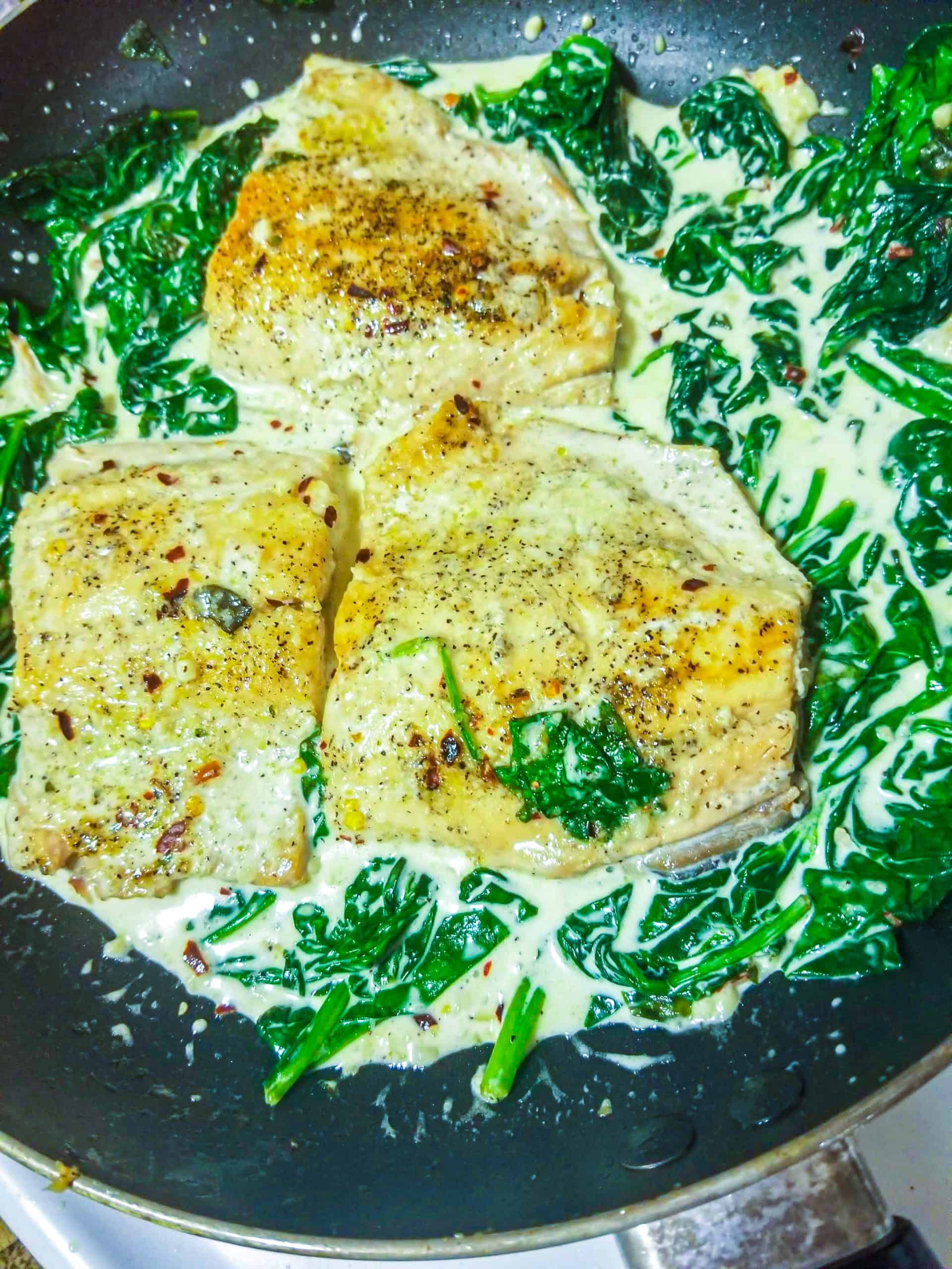 salmon with spinach cream sauce in a pan