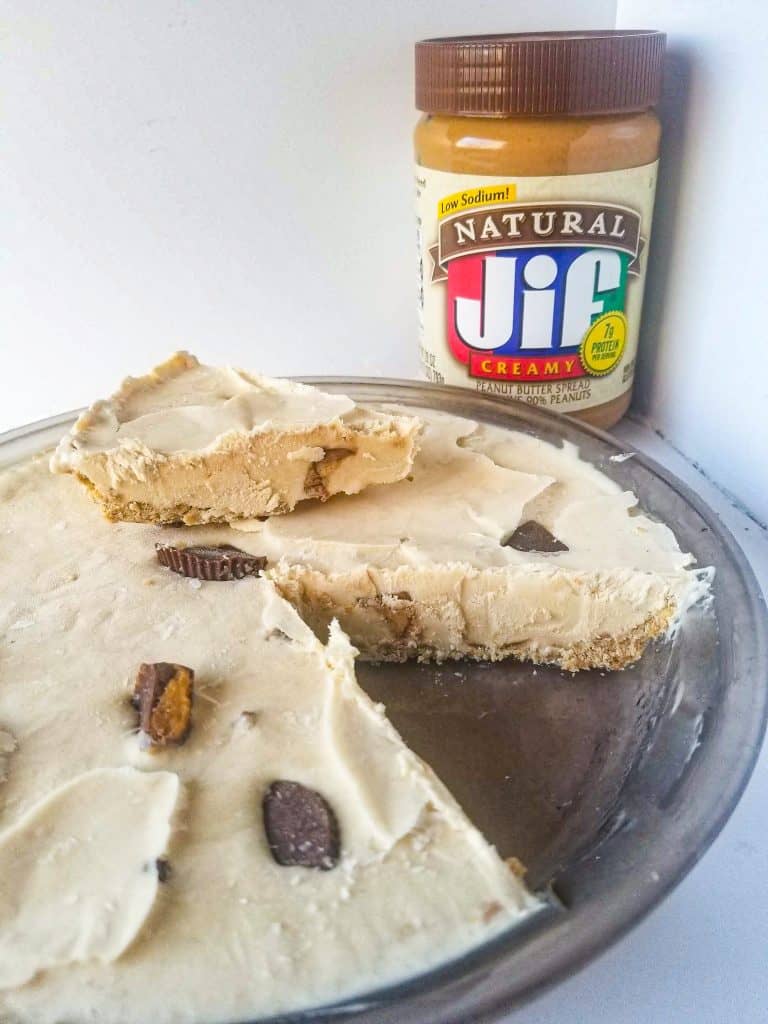 Reese's peanut butter pie with heavy cream in a pie pan with a jar of peanut butter in the background. 