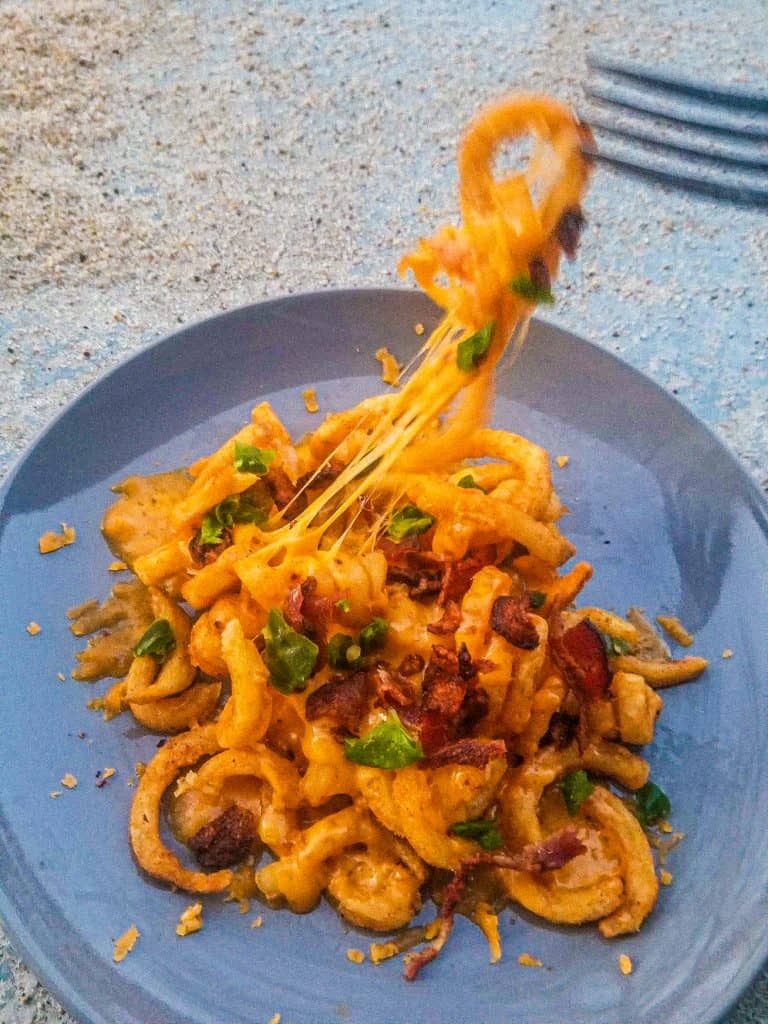 loaded cheesy fries on a gray plate with a fork doing a cheese pull. 