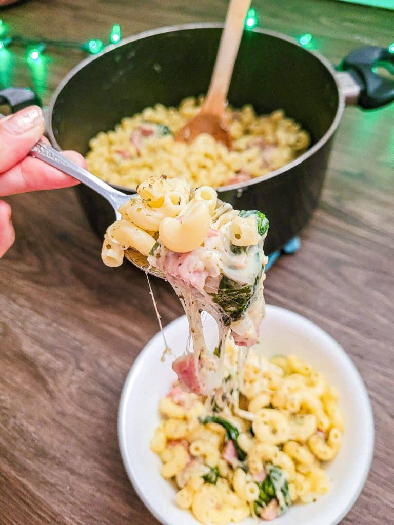 cheese pull of pasta with pot of spinach and sausage pasta in the background.