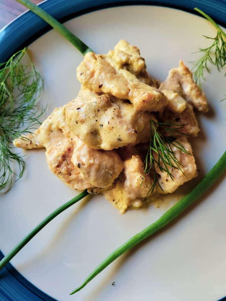 chicken in white sauce on a plate with rosemary sprigs. 