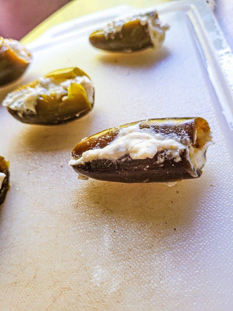 jalapenos with cream cheese on cutting board.
