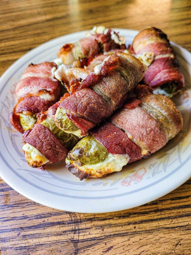 bacon wrapped jalapenos on a plate on a brown table. 