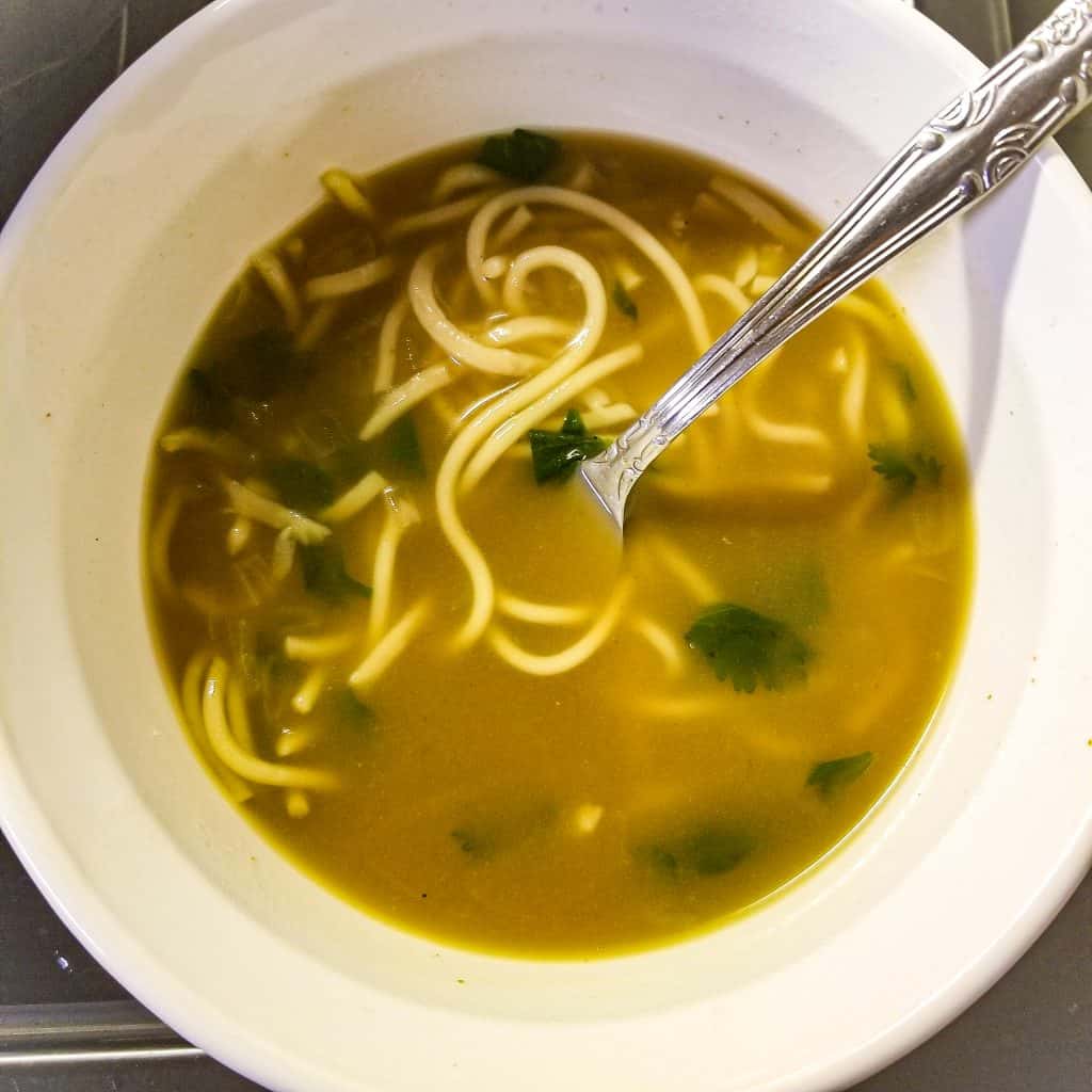 chinese noodle soup in a white bowl with a silver fork.