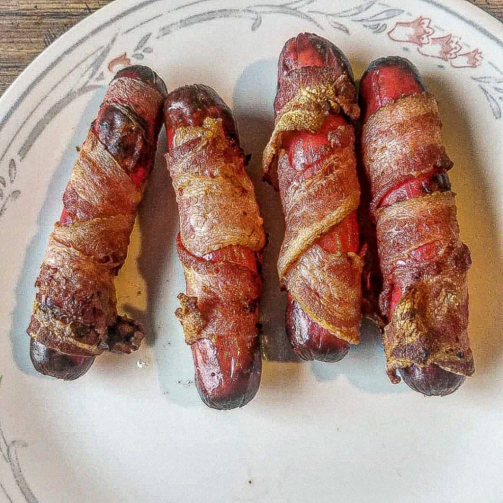bacon wrapped hot dogs on a plate on the table. 