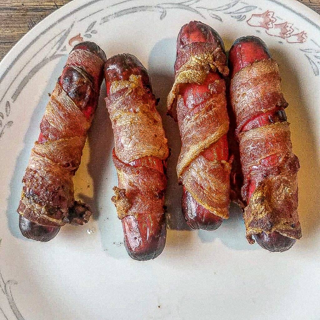 bacon wrapped hot dogs on a plate on the table.