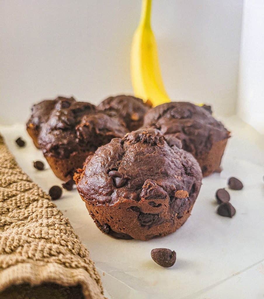 double chocolate chip banana muffins with a banana in the background. 