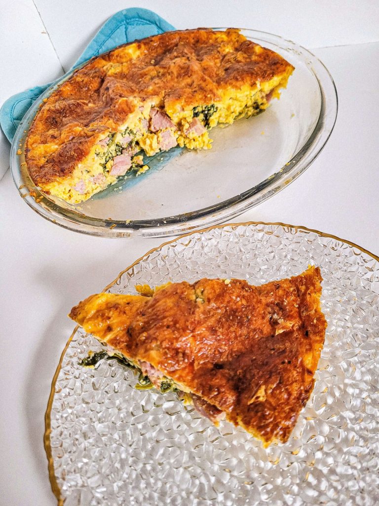 ham and spinach quiche in a glass pan from the side view.
