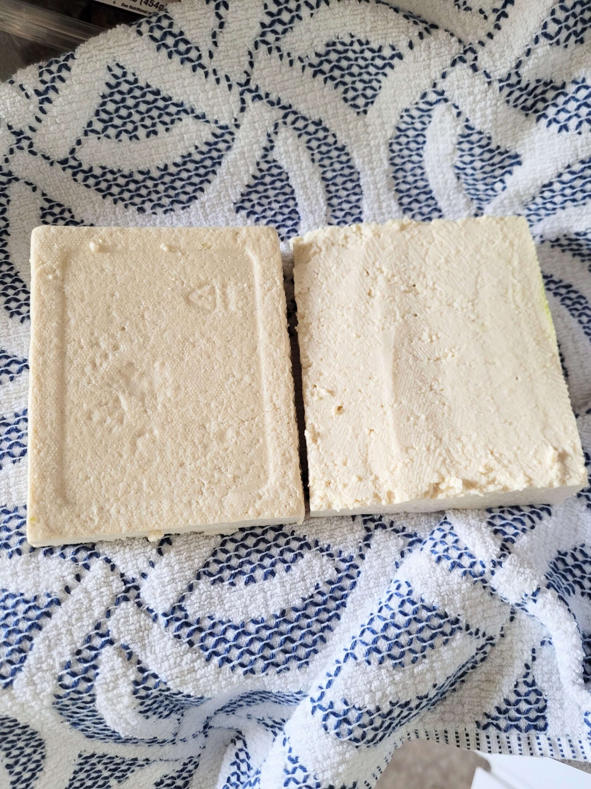 two slabs of tofu on a clean white and blue kitchen towel
