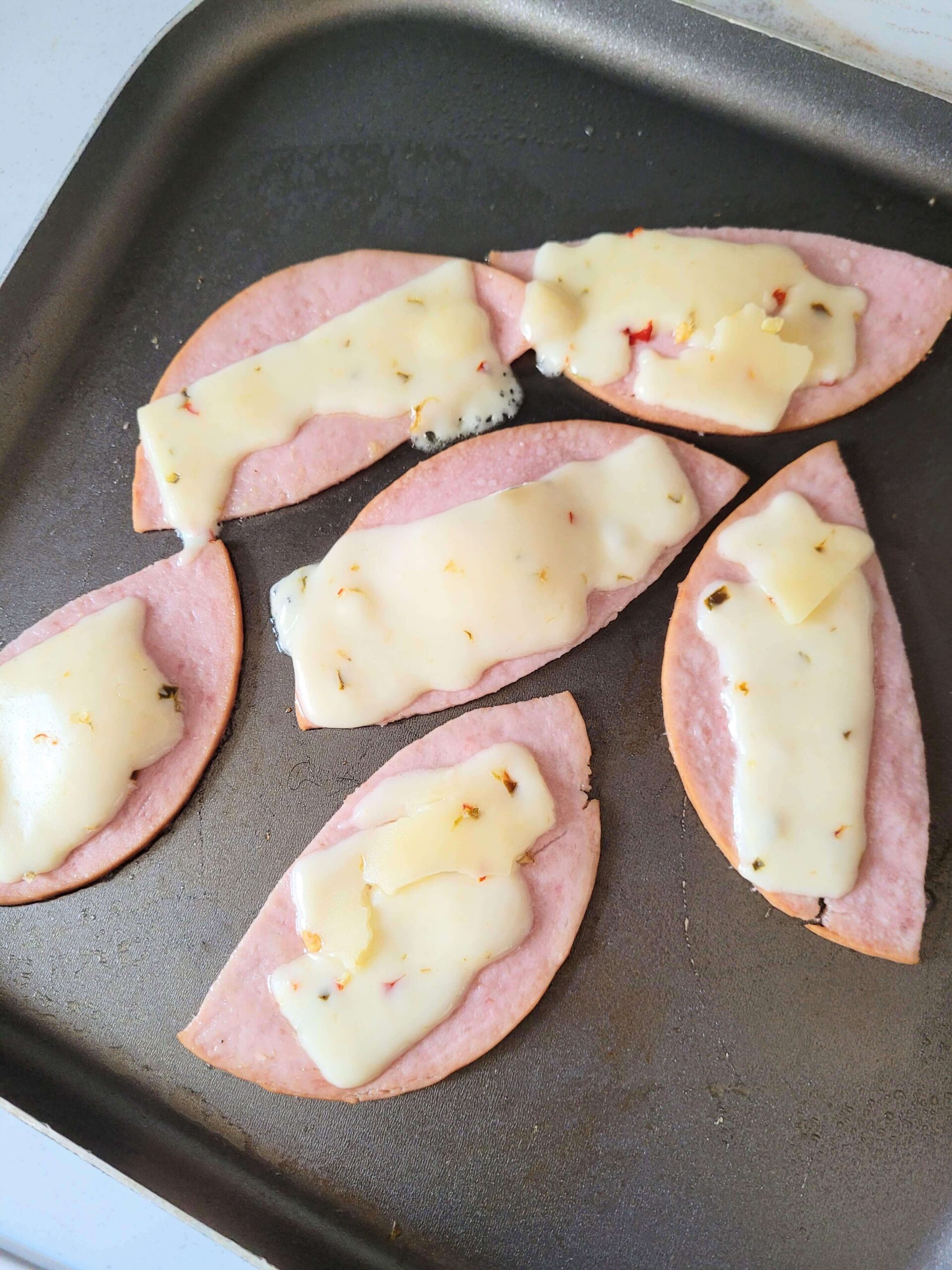 lunch meat cut into strips with cheese melted on top in a black frying pan.