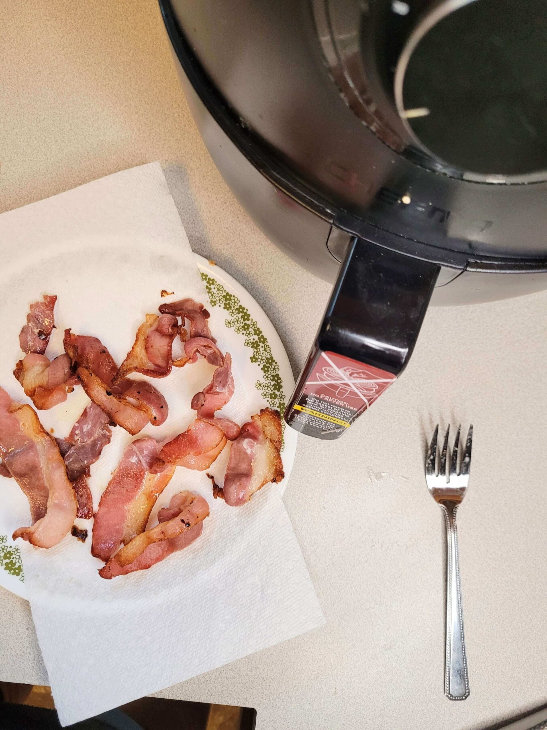 Bacon on paper towel with fork and air fryer in background.
