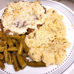 Cream cheese mashed potatoes with green beans and country fried cube steak on a plate.