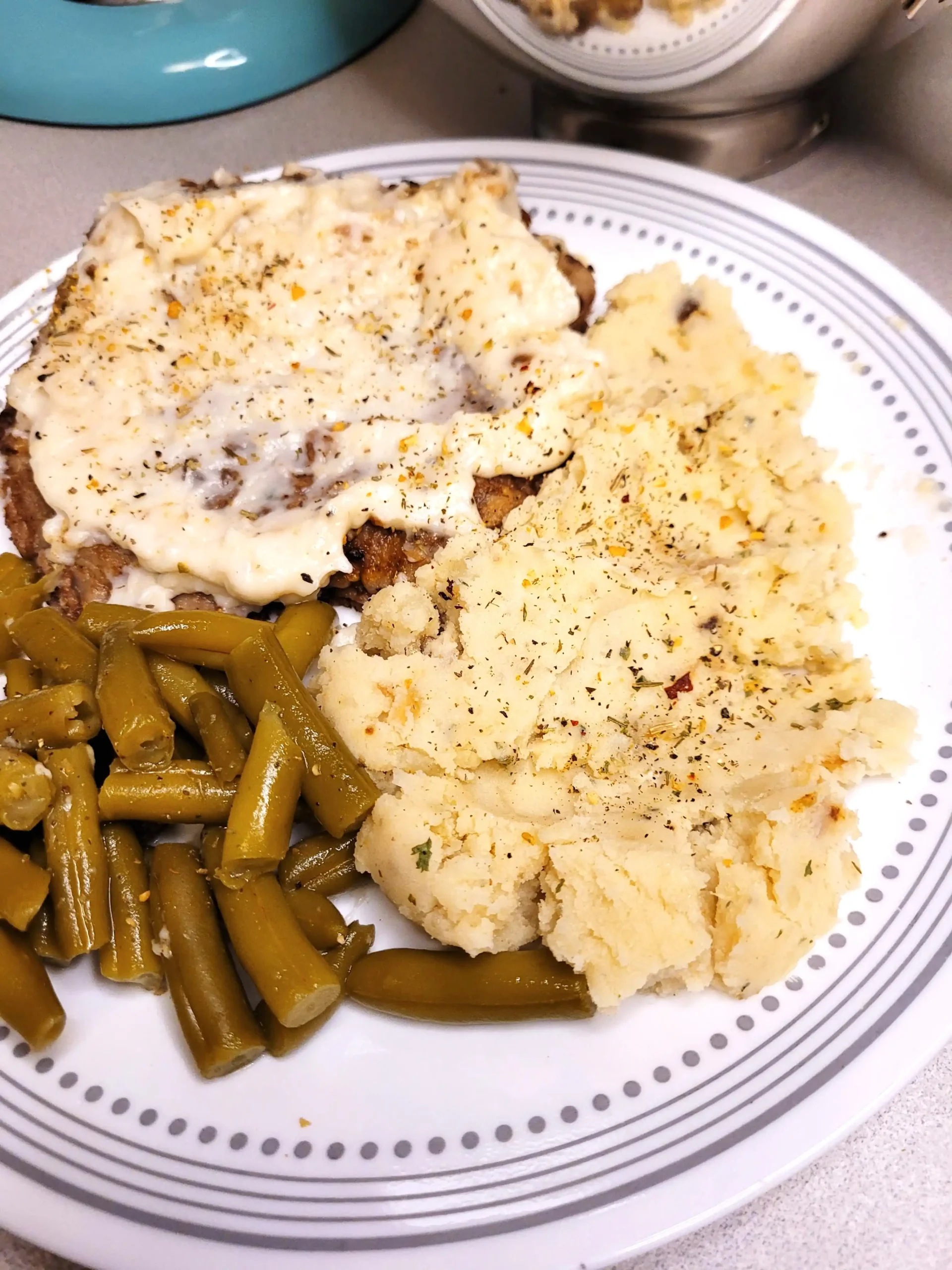 Cream cheese mashed potatoes with green beans and country fried cube steak on a plate.
