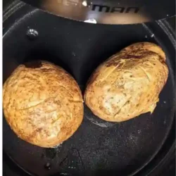 Two cooked baked potatoes sitting in air fryer.