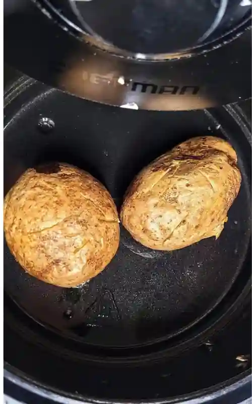 Two cooked baked potatoes sitting in air fryer.