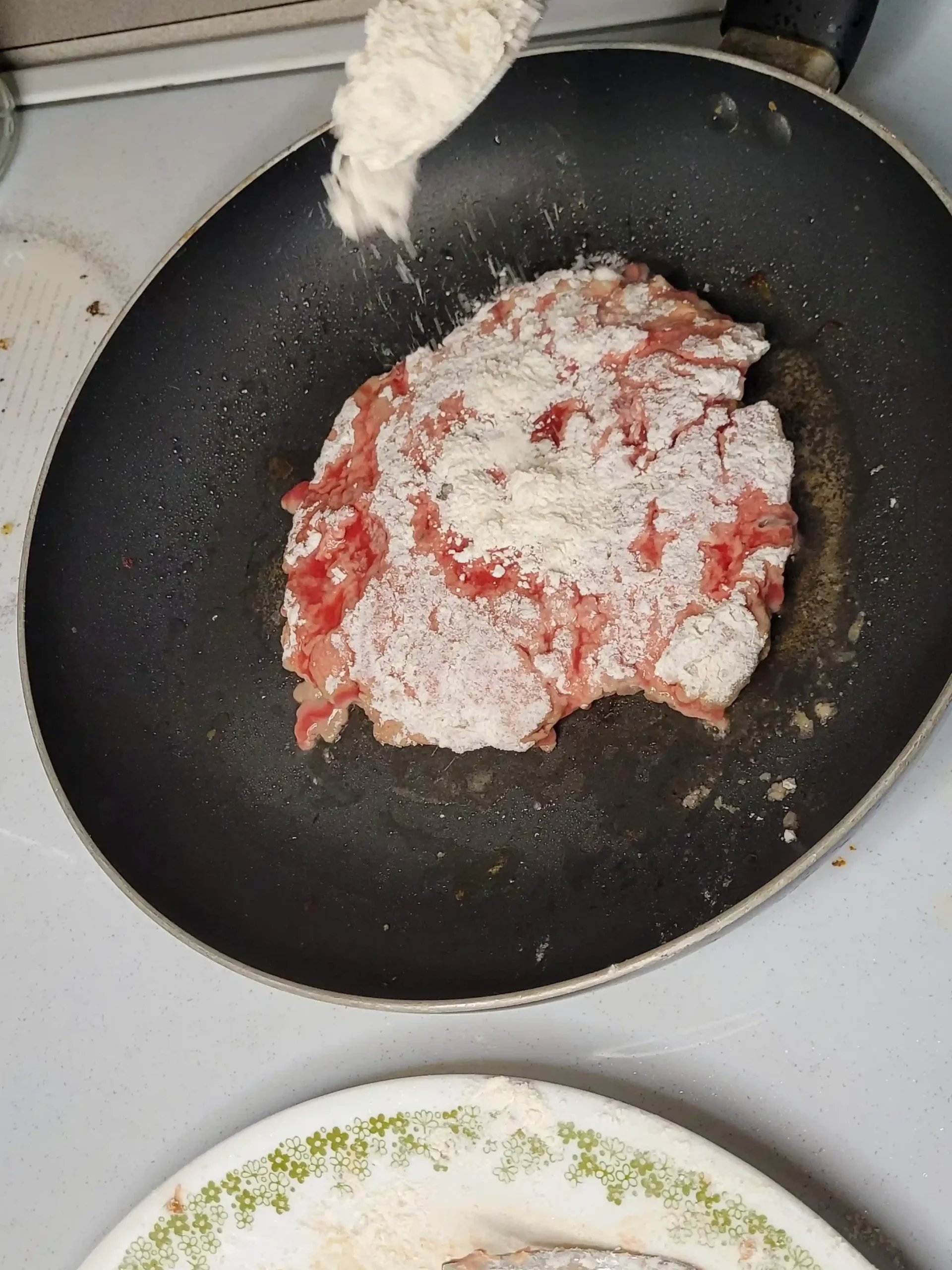 spoon adding extra flour on top of cooking meat on stove.