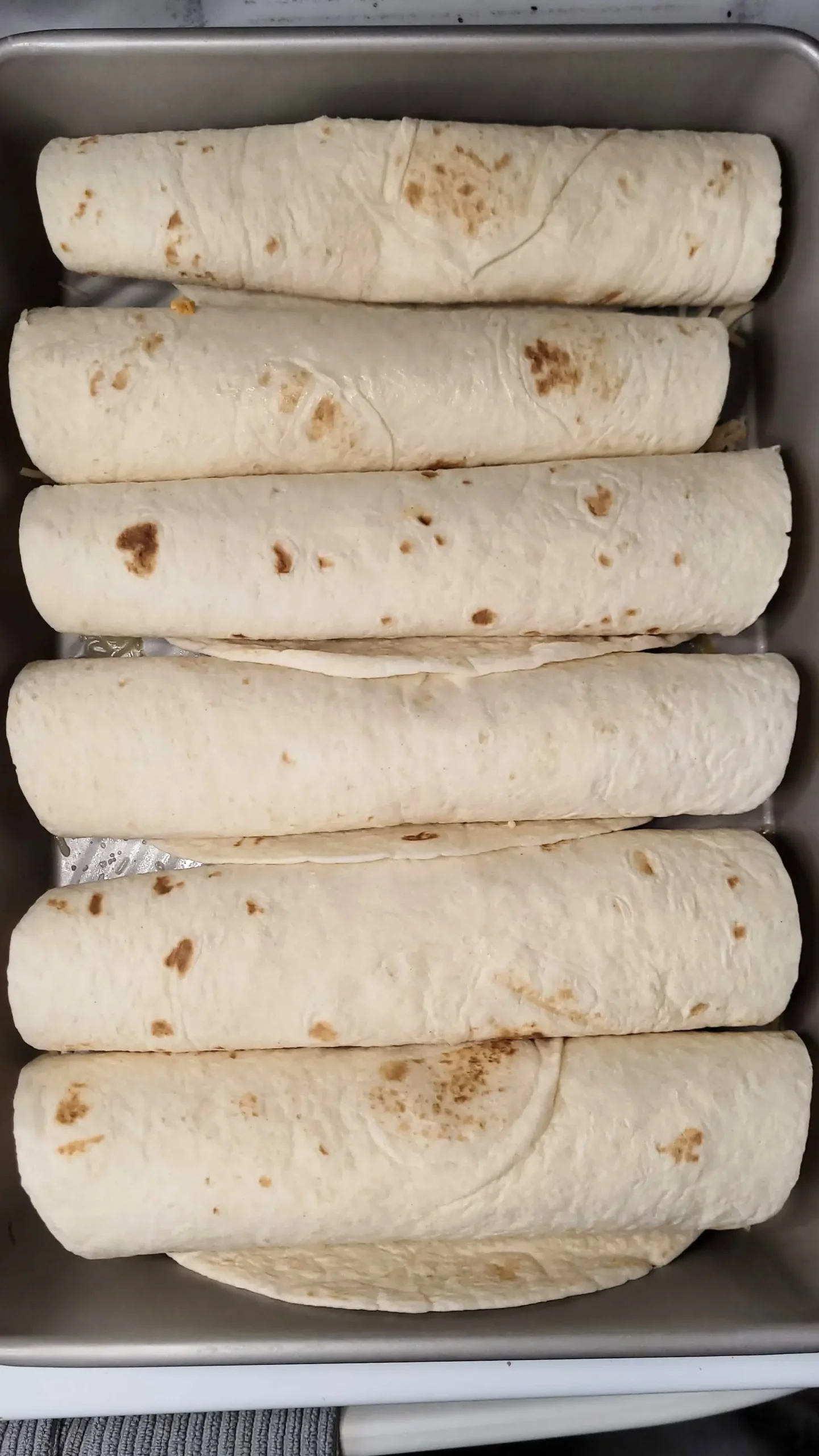 Rolled enchilada tortillas in pan.