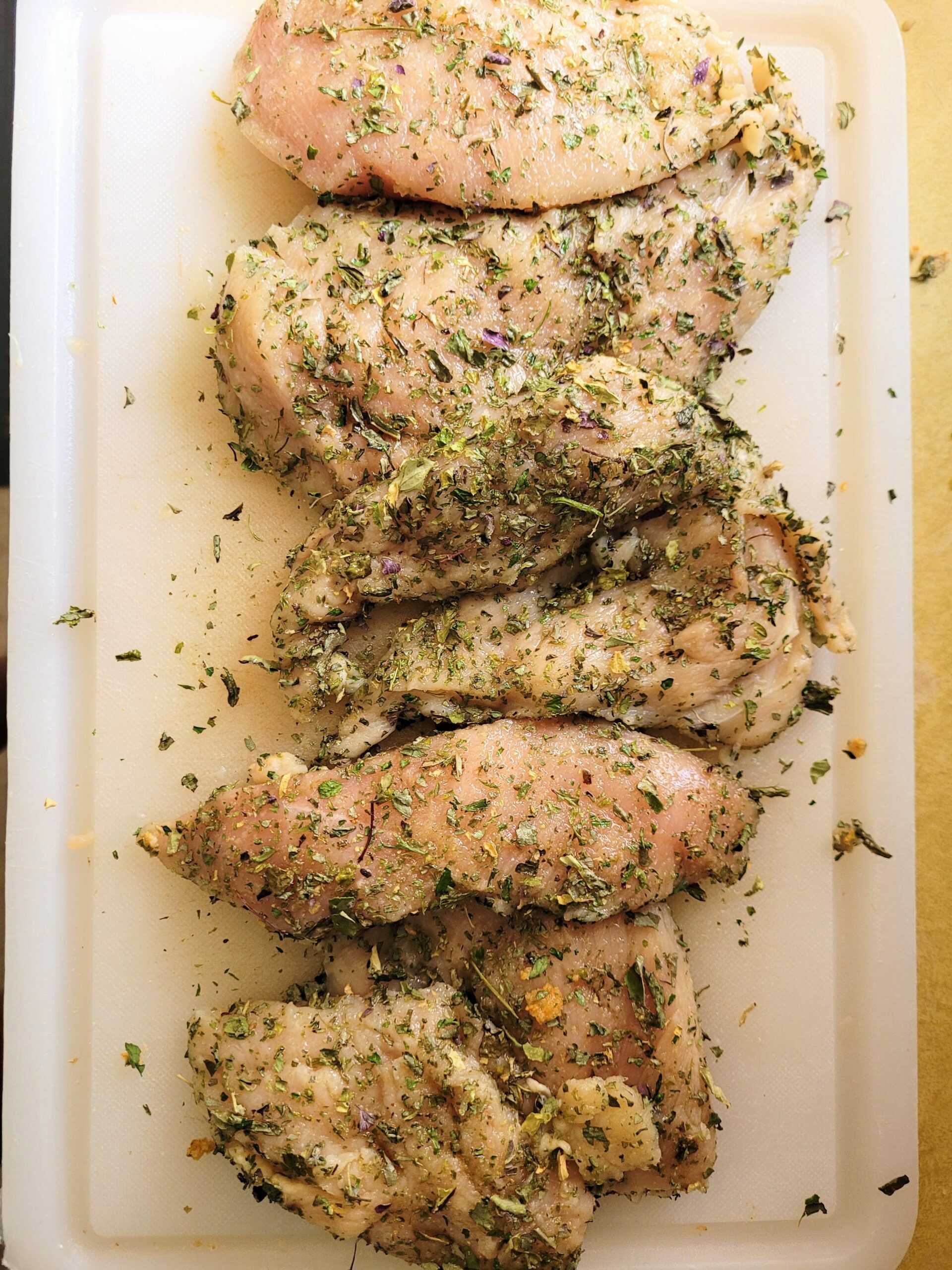 herb seasoning on chicken bread on a white cutting board.