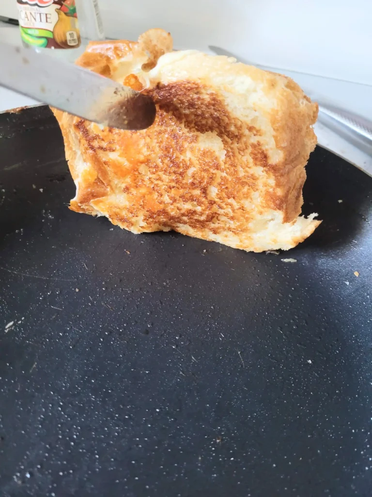 Knife lifting up grilled ham and cheese in pan. 