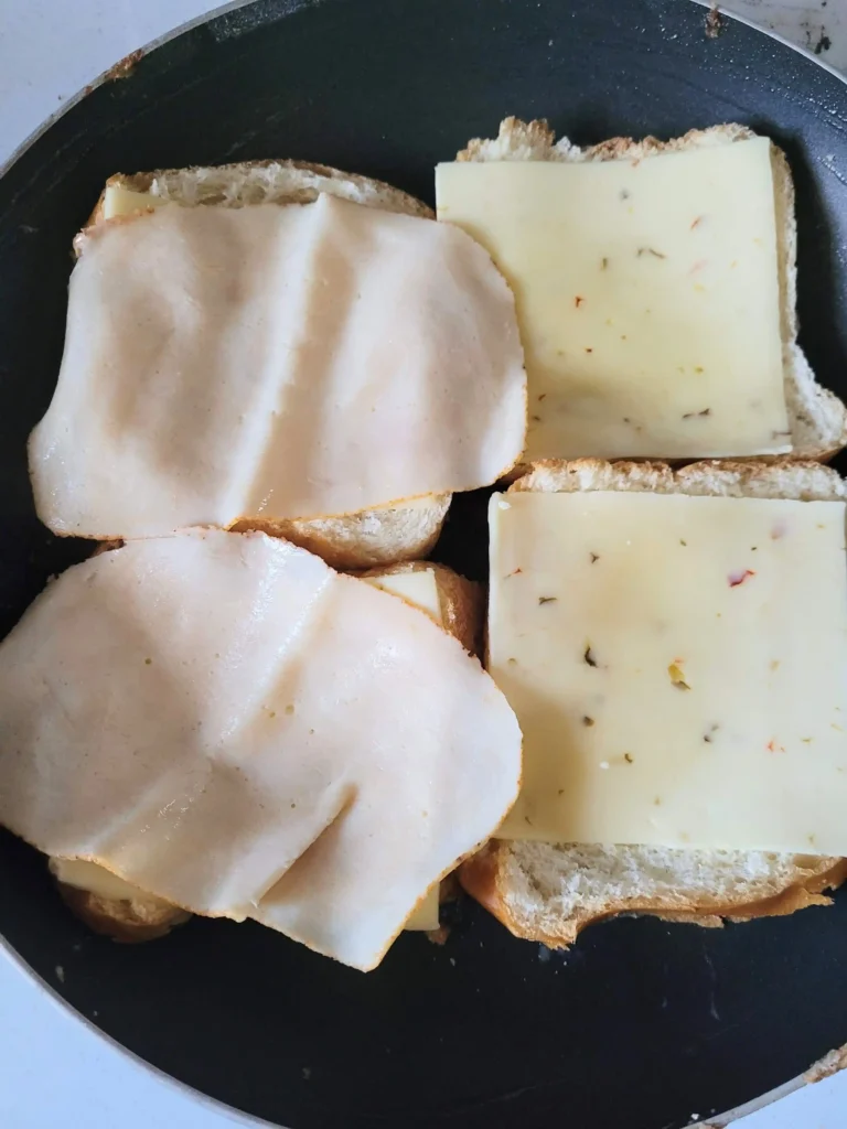 Bread frying in pan with ham and cheese on top.