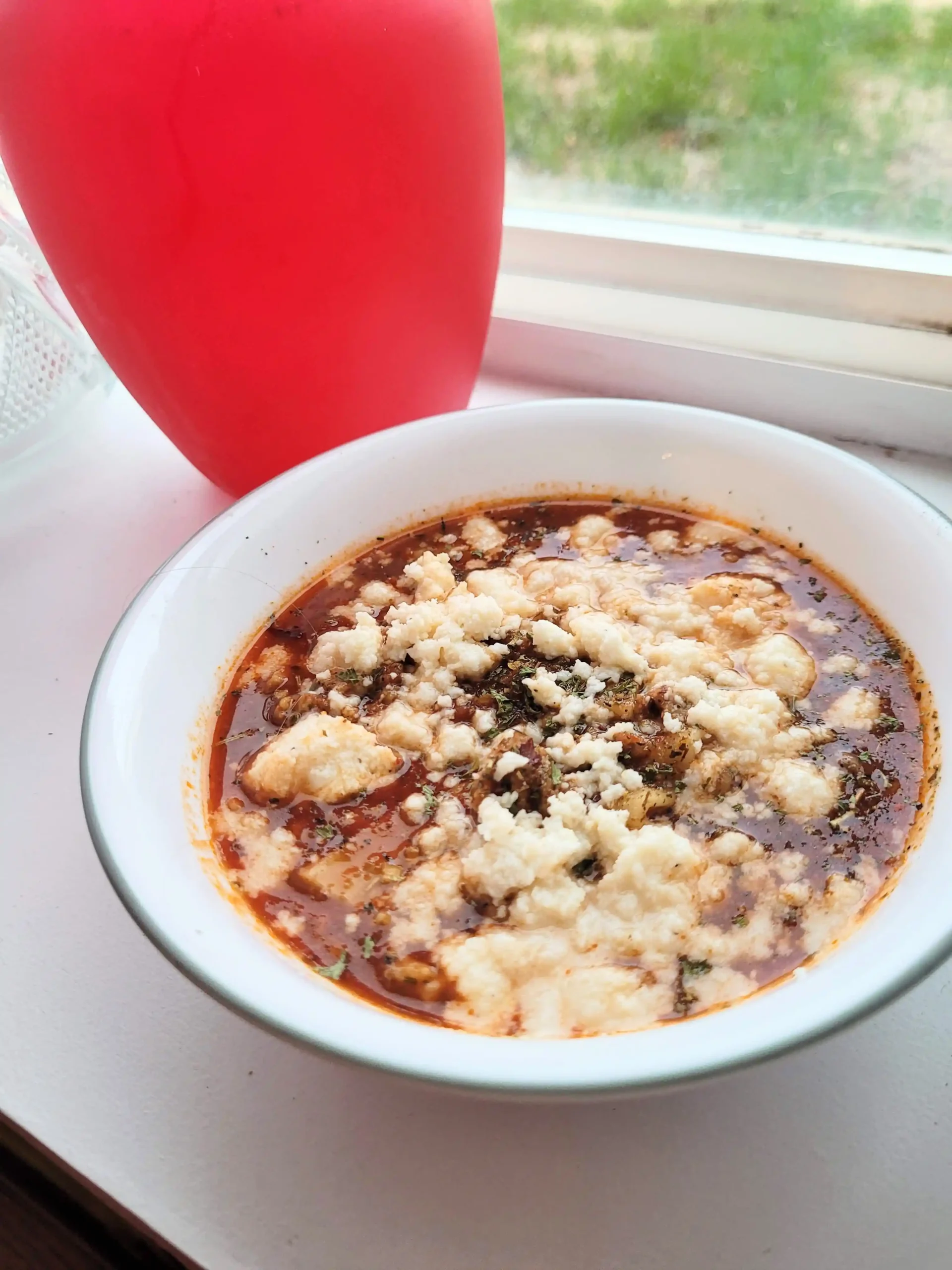 Lasagna soup with cheese on top with pink vase in background.