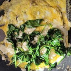 Omelet frying in skillet with spinach and cheese on top.